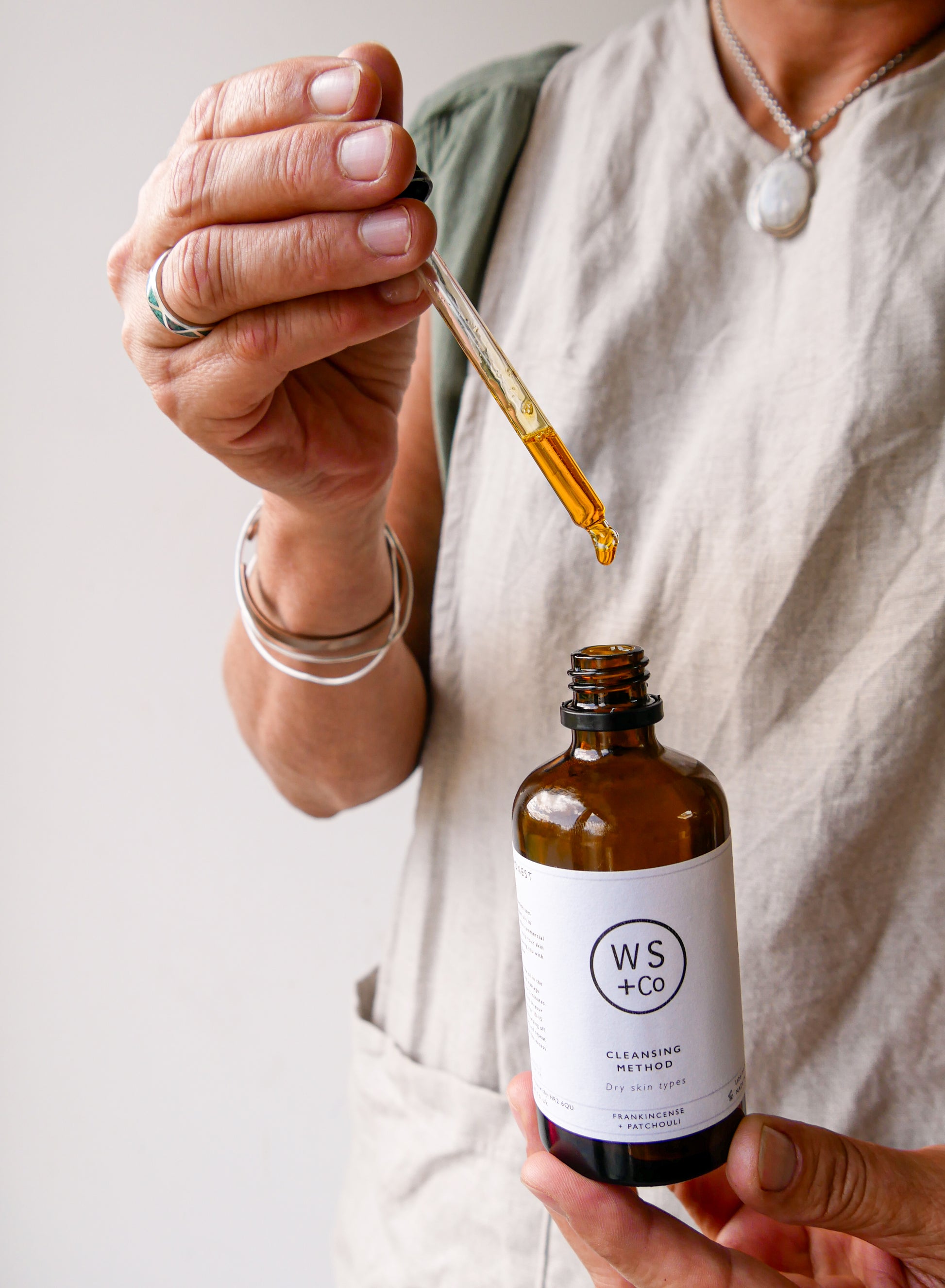 Julie holding a dropper with oil over a bottle labeled 'WS+Co' against a neutral background