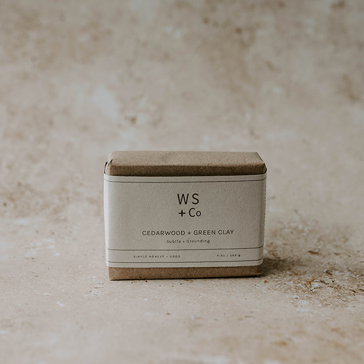 A bar of handmade soap with a label that reads 'WS + CO Cedarwood & Green Clay' placed on a textured surface.