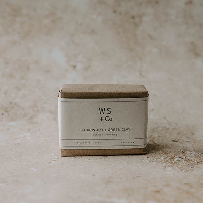 A bar of handmade soap with a label that reads 'WS + CO Cedarwood & Green Clay' placed on a textured surface.