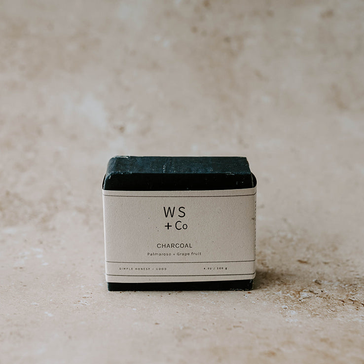 A packaged charcoal soap bar with the brand name WS + Co visible on the label, placed on a textured background.