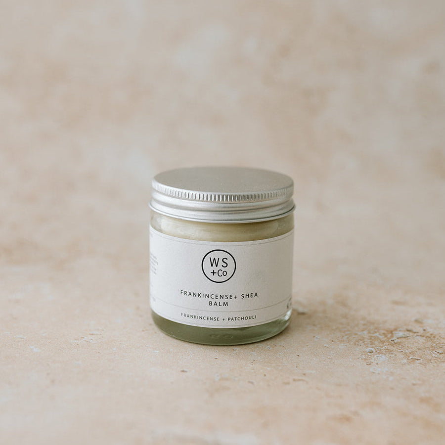 Small jar of balm with a visible brand logo on a textured beige background