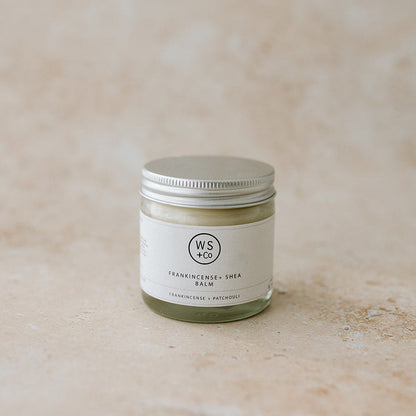 Small jar of balm with a visible brand logo on a textured beige background