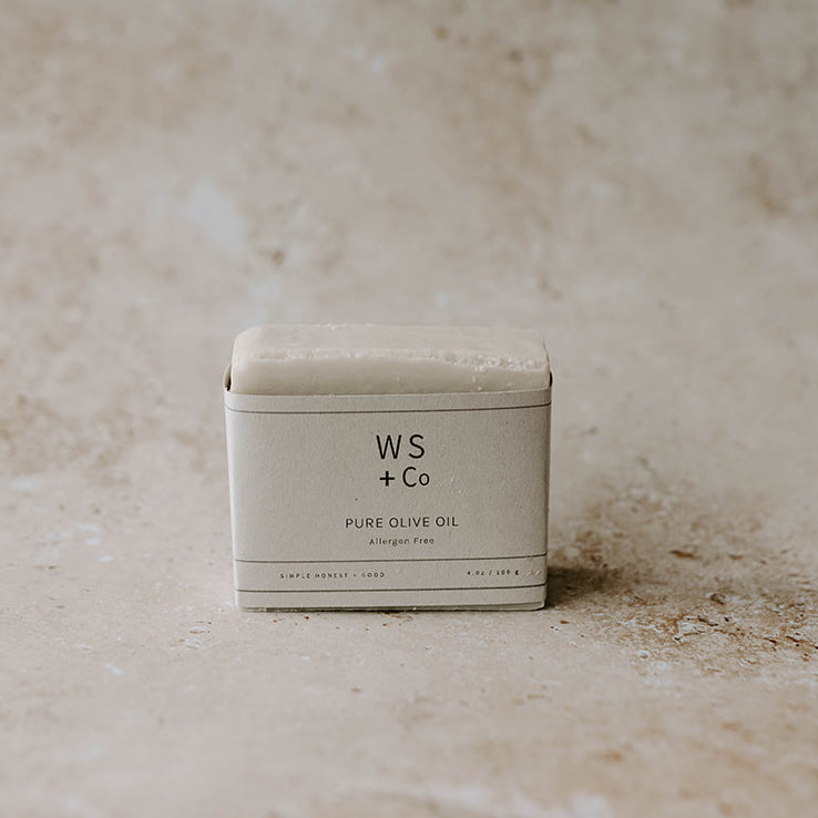 A bar of soap with 'WS + Co PURE OLIVE OIL' printed on it, placed on a textured background.