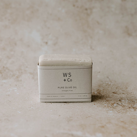 A bar of soap with 'WS + Co PURE OLIVE OIL' printed on it, placed on a textured background.