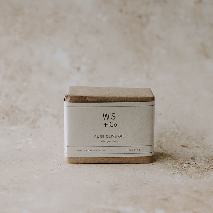 A bar of soap with a label that reads 'WS + CO Pure Olive Oil', placed on a textured beige surface.