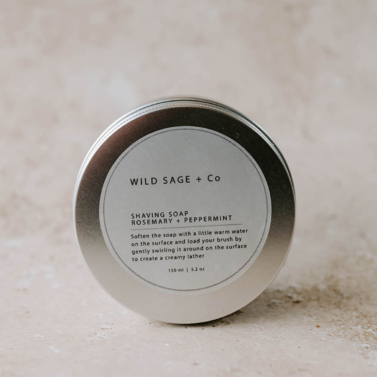 A metal tin container with a label that reads 'WILD SAGE + CO SHAVING SOAP Rosemary + Peppermint'.