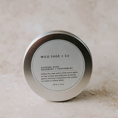 A metal tin container with a label that reads 'WILD SAGE + CO SHAVING SOAP Rosemary + Peppermint'.
