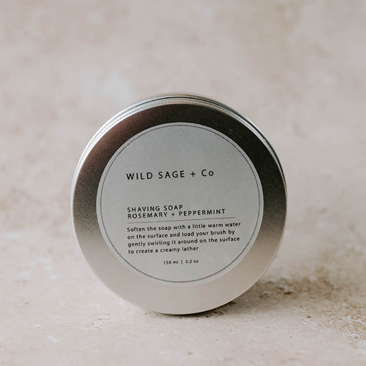 A metal tin container with a label that reads 'WILD SAGE + CO SHAVING SOAP Rosemary + Peppermint'.