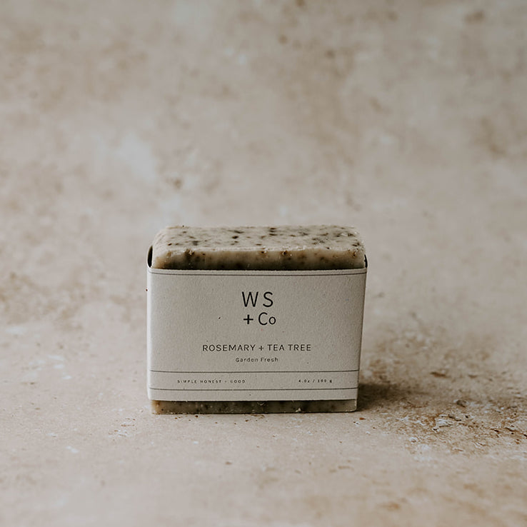 A bar of Rosemary + Tea Tree soap with exfoliants, packaged in a simple white box with the brand WS + Co visible.
