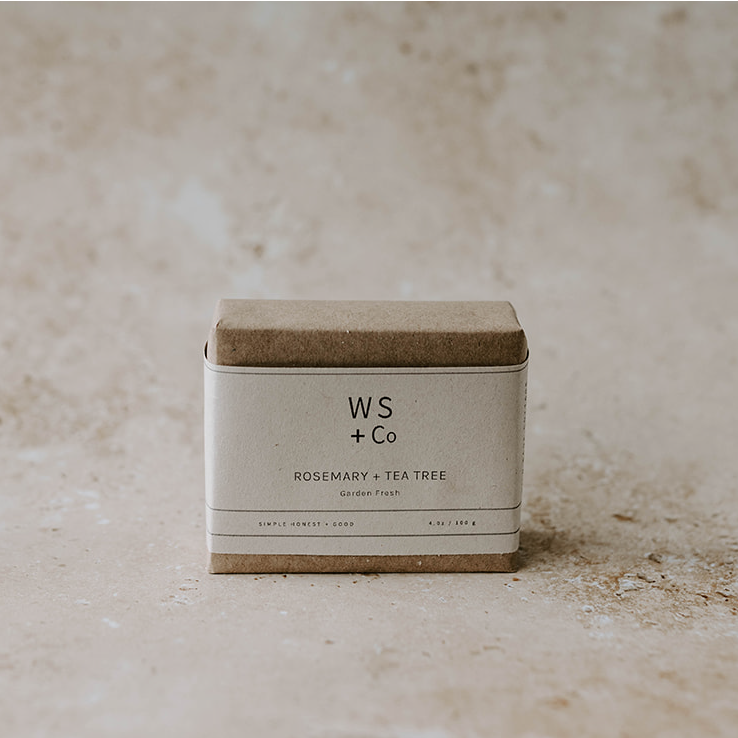 A bar of soap with a label that reads 'WS + CO Rosemary Tea Tree' placed on a textured surface with a neutral background.