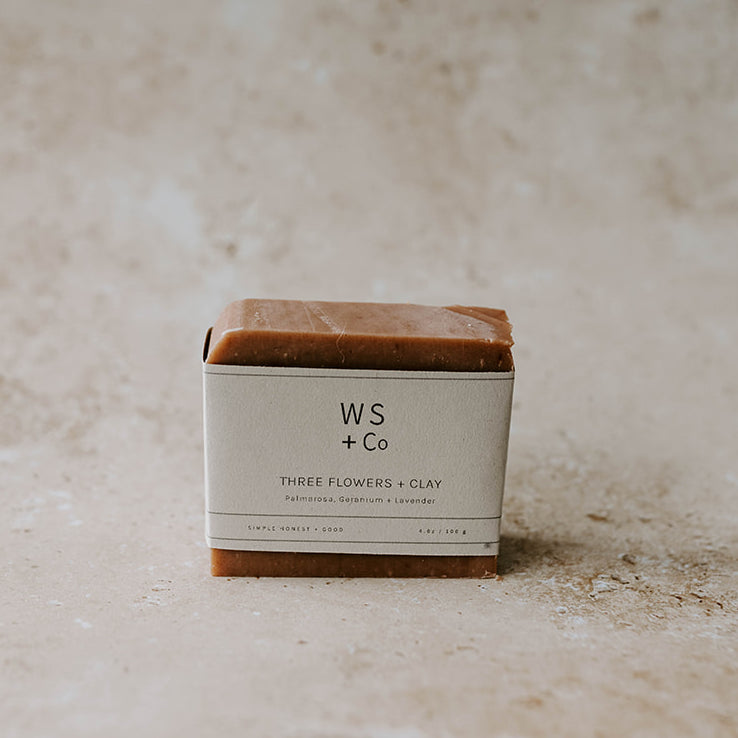 A packaged bar of soap labeled 'WS + Co THREE FLOWERS + CLAY' on a textured background.